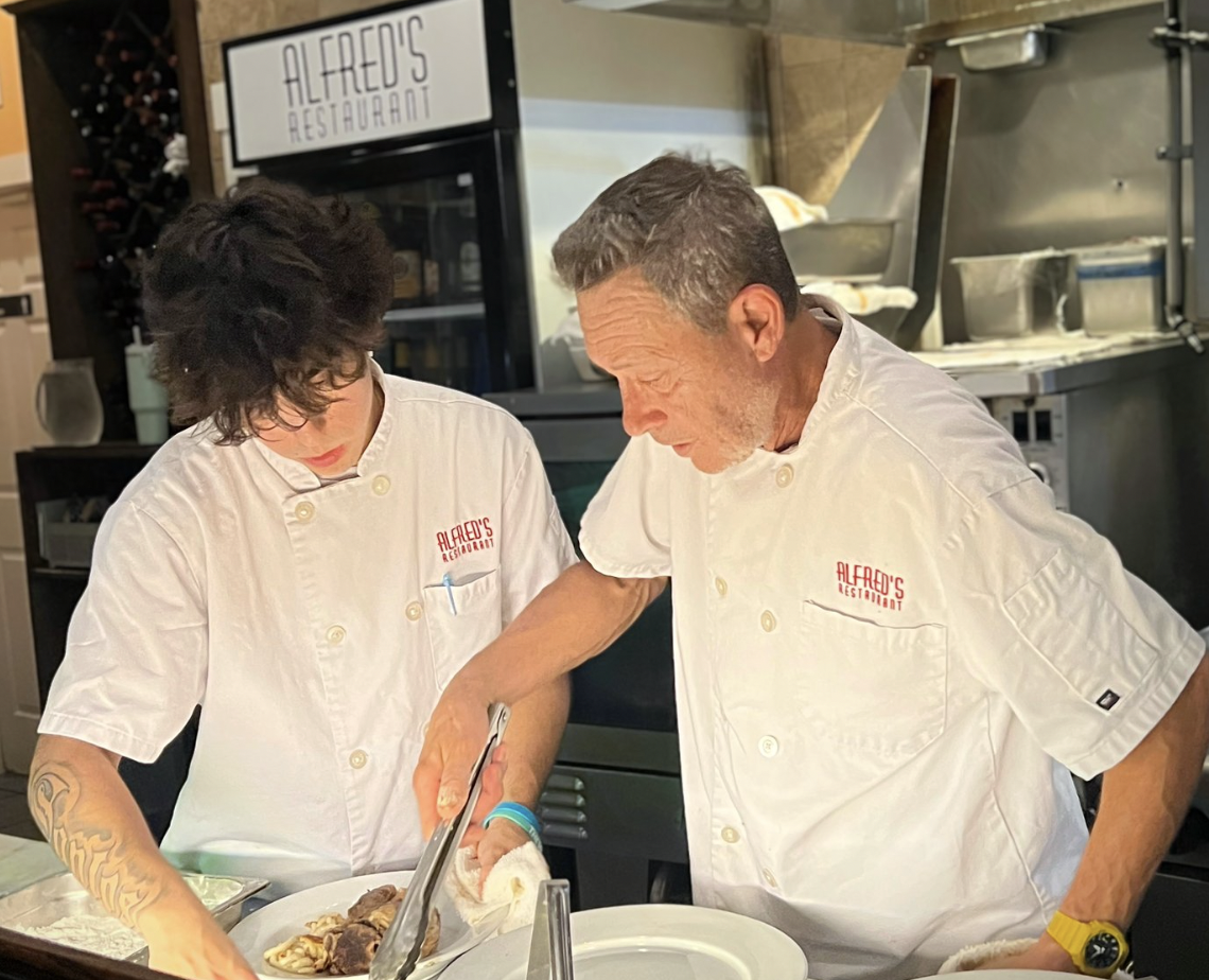 Deux chefs cuisiniers en vestes blanches d'Alfred's Restaurant préparant des plats dans une cuisine professionnelle.